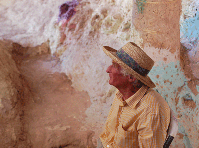 An elderly man sits in front of a mural