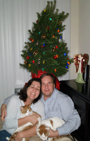 A couple, each holding a cat, near a Christmas tree